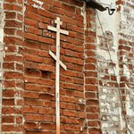 Деревянный православный крест из дощечек на замурованном кирпичном окне.